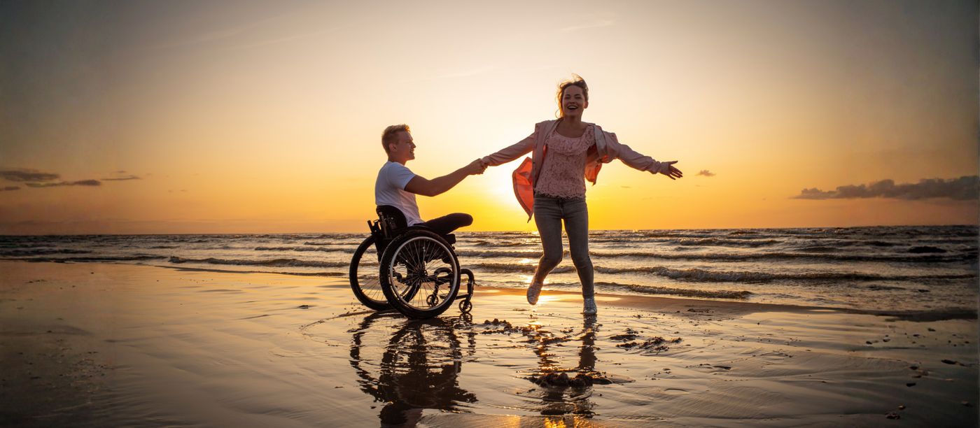 A couple at the water's edge at sunset, one using a wheelchair