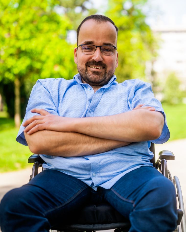 A man in a park, arms folded, wheelchair user, looking at the camera