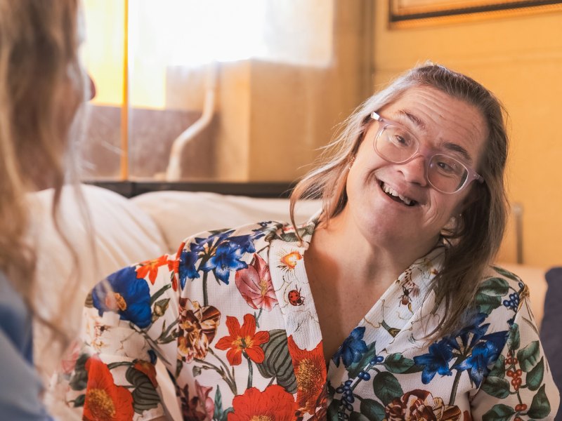 Two people sitting together and laughing, one wearing glasses and a floral shirt