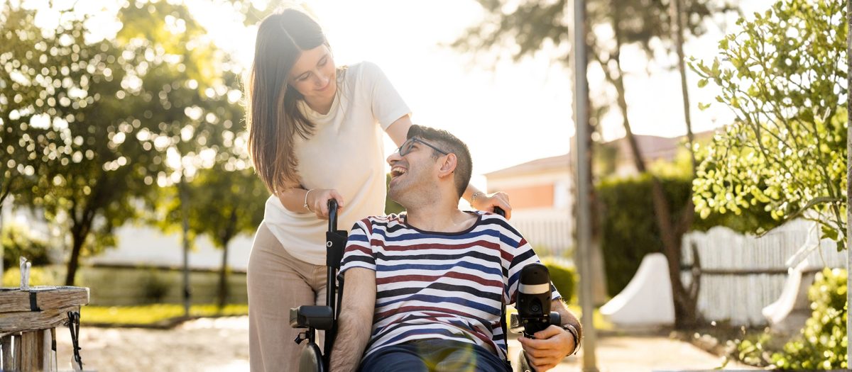 A couple sitting close together outdoors, one using a wheelchair